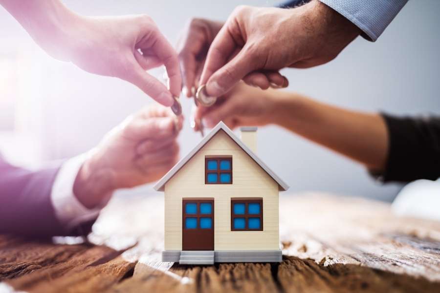 Deux personnes déposant des pièces sur un modèle de maison miniature symbolisant un investissement immobilier commun.
