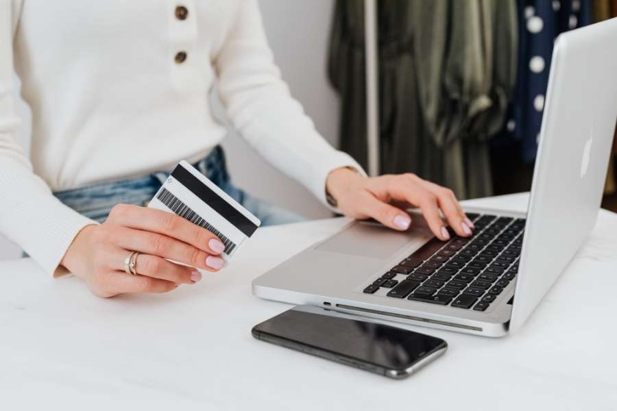 Une femme tient une carte bancaire tout en effectuant un achat sur son ordinateur portable.